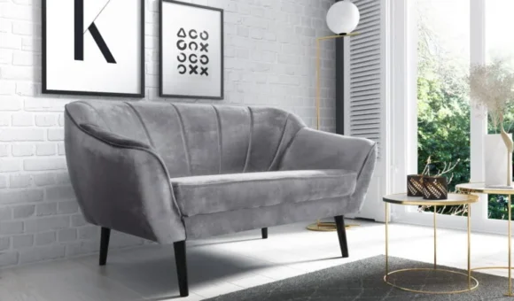 Szara dwuosobowa sofa w małym salonie z ceglaną ścianą